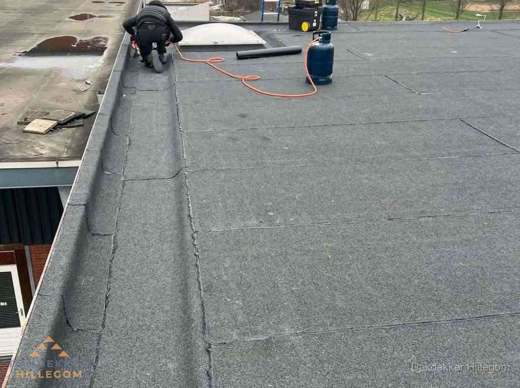 Dakdekker repareert bitumen dakbedekking op groot plat dak in Hillegom
